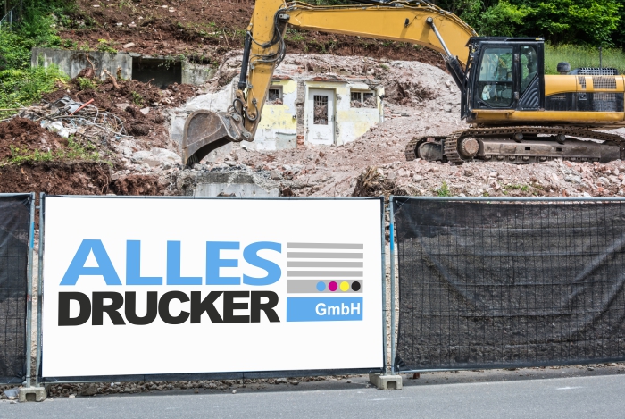 Bedruckte Bauzaunplane mit dem Allesdrucker GmbH Logo vor einer baustelle mit einem großen weißem Bagger